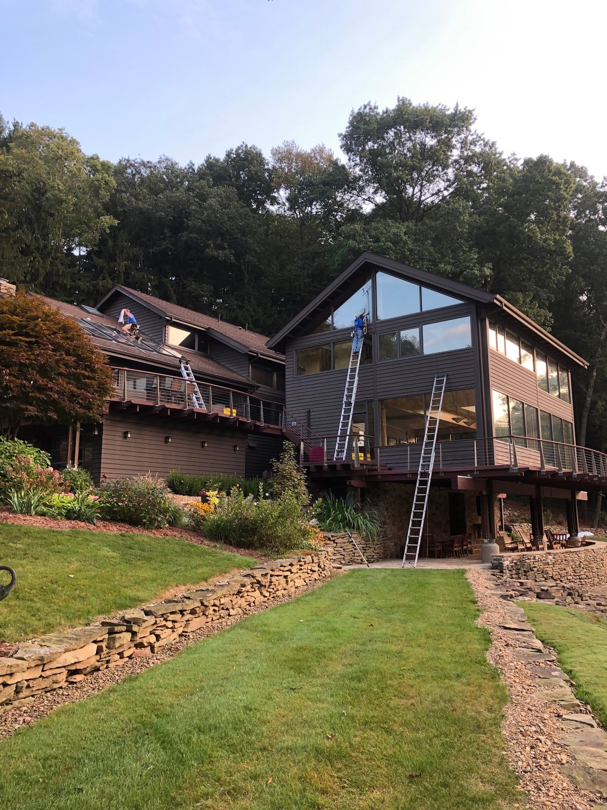 Modern multi-level home with large windows and decking elevated on stilts, surrounded by landscaped grounds and mature trees