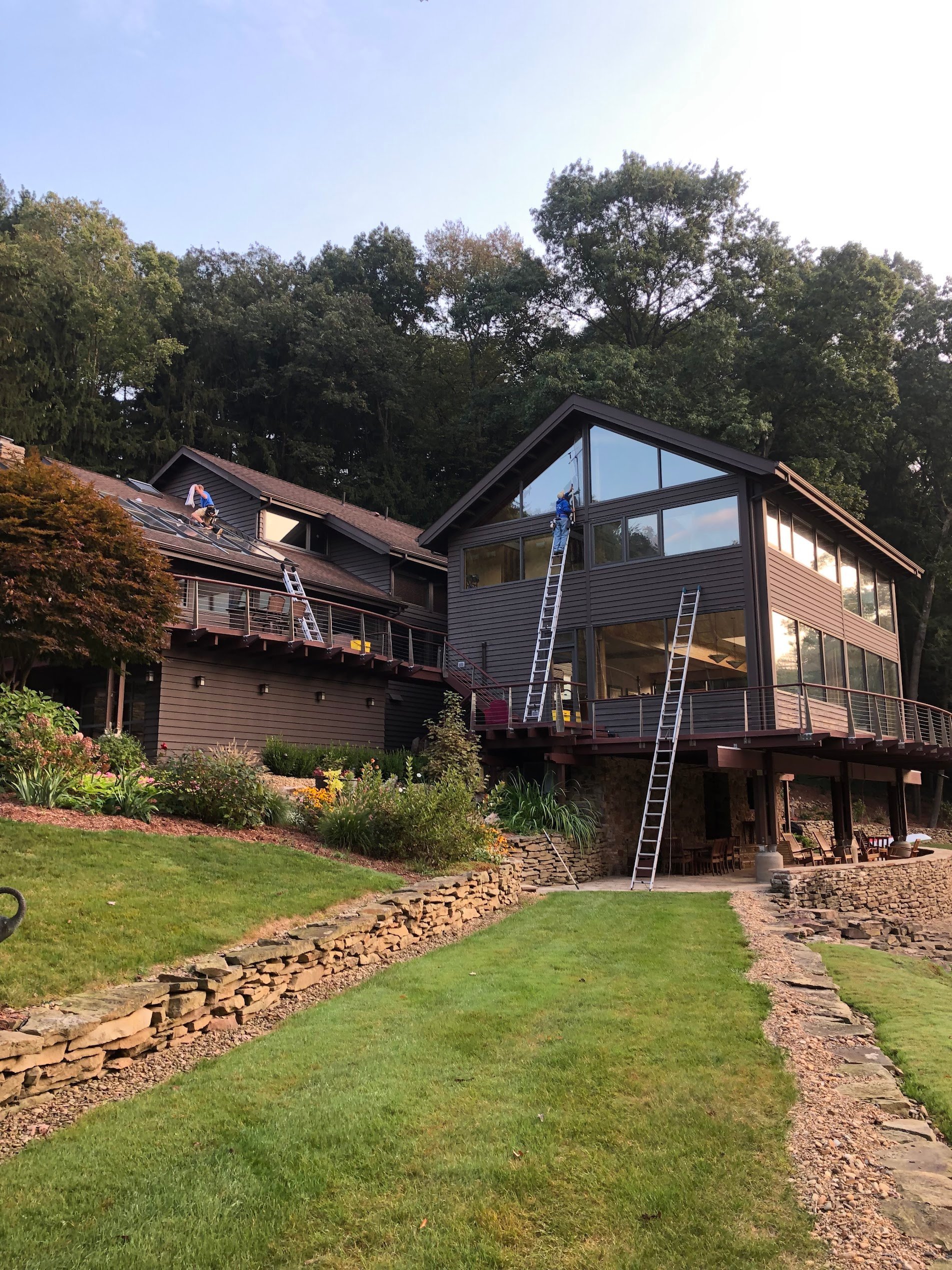 Modern multi-level home with large windows and decking elevated on stilts, surrounded by landscaped grounds and mature trees