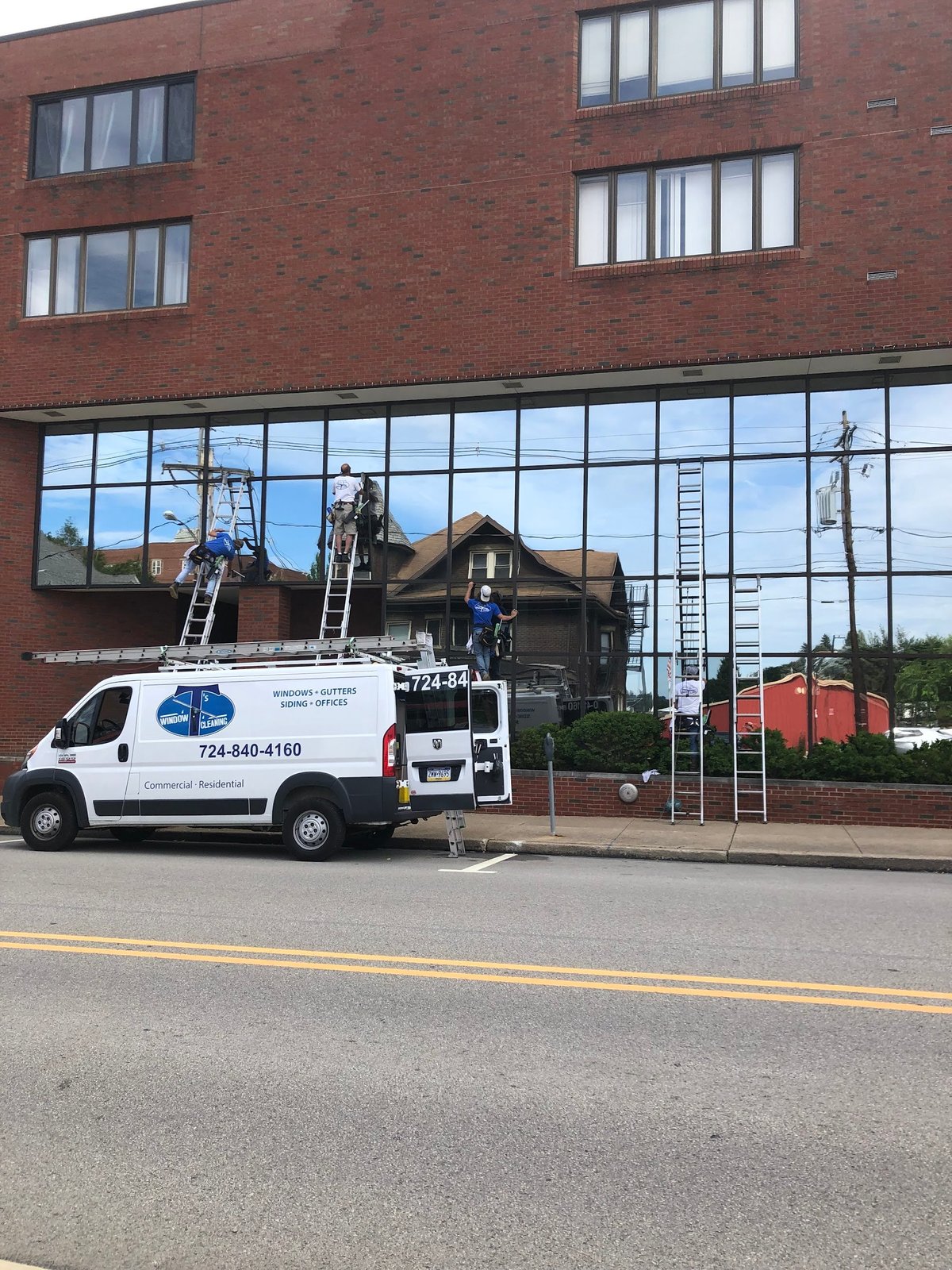 Window cleaning service truck with extended ladder and boom equipment parked in front of a brick building with large storefront windows